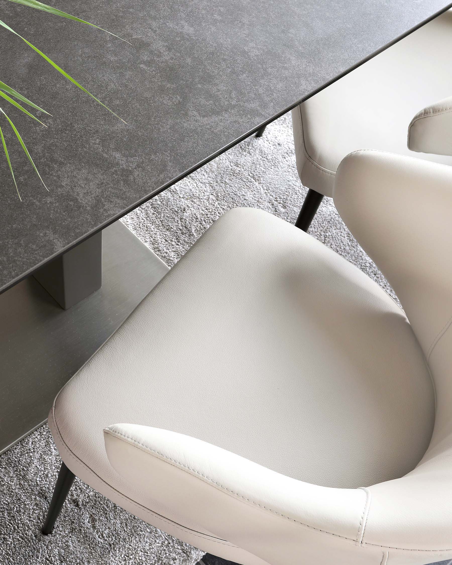 Modern dining furniture featuring a dark grey stone tabletop with sleek, straight metal legs, paired with an elegant light grey upholstered chair with a curved backrest and slender black metal legs, set on a textured grey area rug.