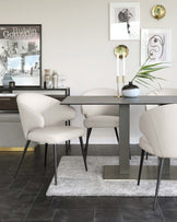 Modern minimalist dining set featuring a sleek, rectangular table with a matte grey finish and sturdy metal legs, paired with four elegant, curved-back chairs upholstered in cream leather with slender black metal legs, all accentuated by a fluffy, grey area rug underneath.