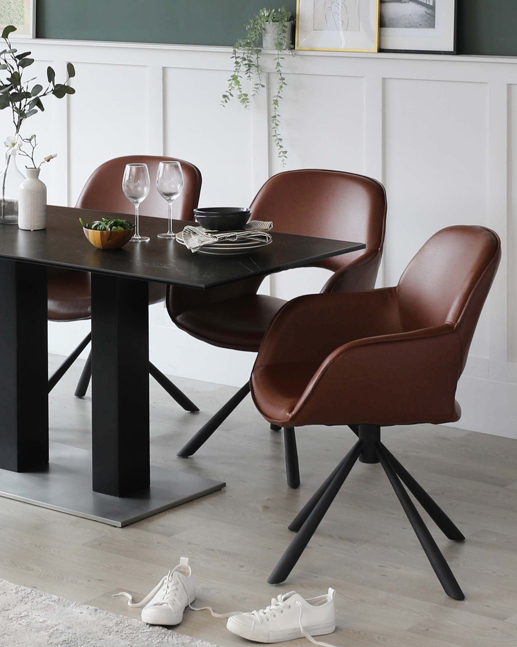 Modern dining room featuring a sleek black rectangular table with sturdy legs and a set of two contemporary chairs with smooth brown leather upholstery and black metal swivel bases.