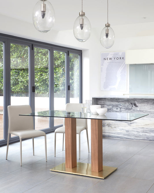 Modern dining set featuring a rectangular glass-top table with a wooden base accented by brass plating, paired with sleek white leather chairs with slender metal legs.