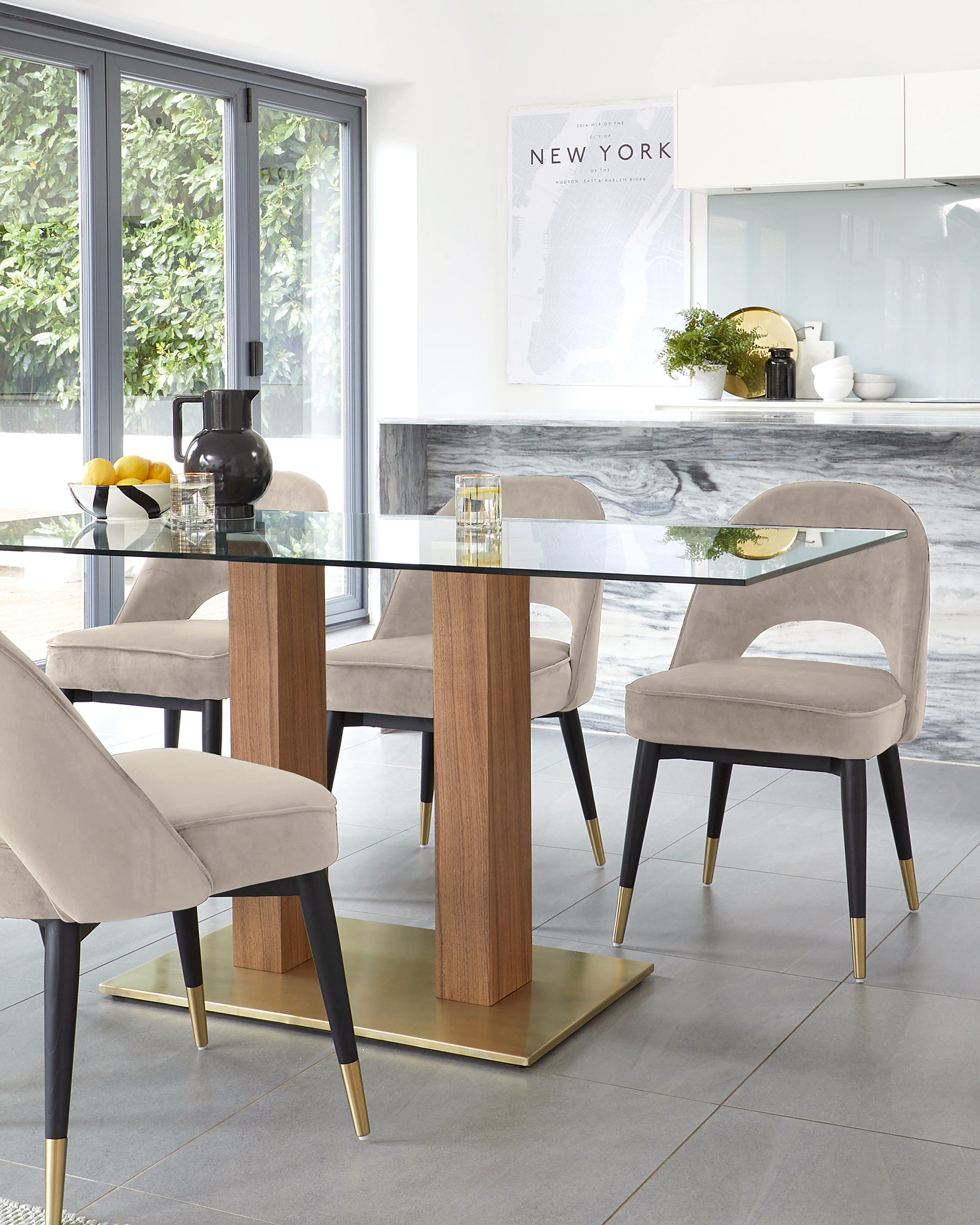 A modern dining set featuring a rectangular glass-top table with sturdy wooden legs and brass-tone accents, complemented by four plush, velvet-upholstered chairs with black and brass legs.