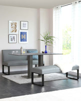 Modern minimalist dining set featuring a matte grey rectangular table with sleek black metal legs, complemented by a matching bench and two stools with cushioned grey upholstery and black metal frames, arranged on a plush grey area rug.