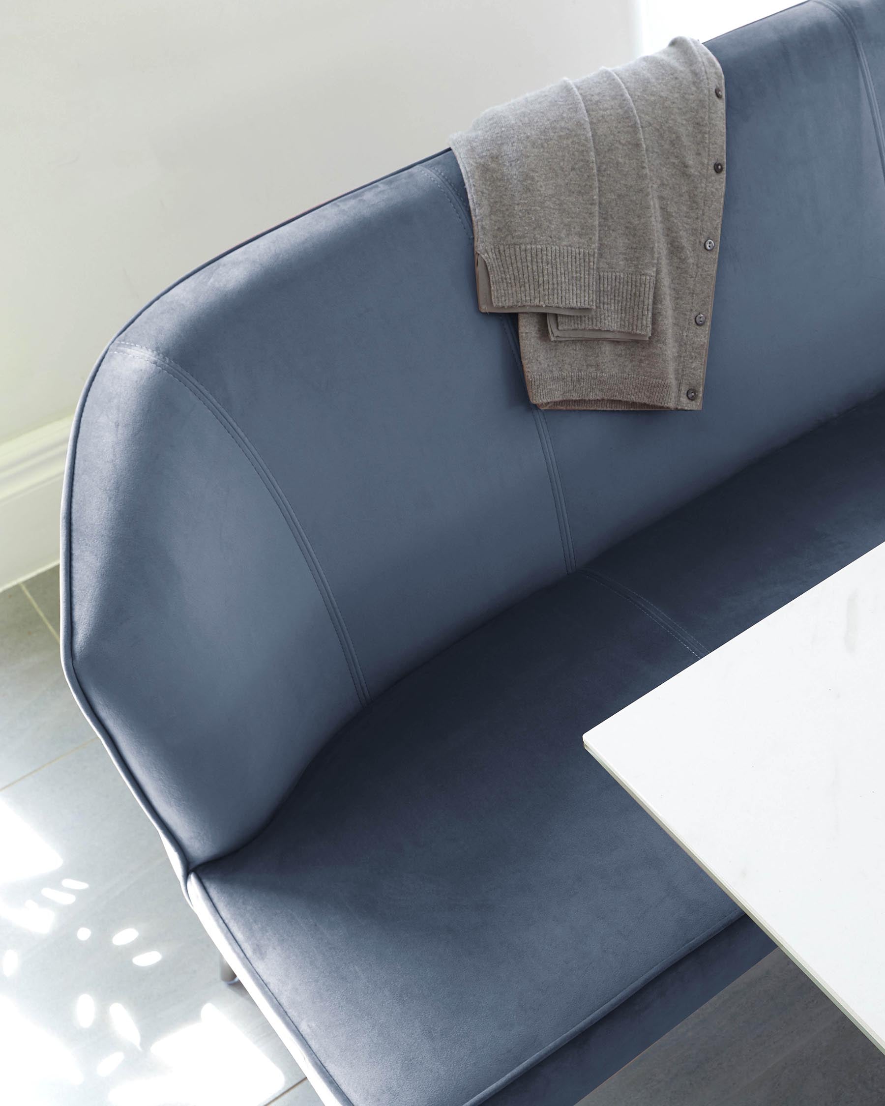 Modern blue upholstered sofa with clean lines and a smooth finish, complemented by a folded grey knit sweater draped over its right corner, set against a serene backdrop with soft natural light.