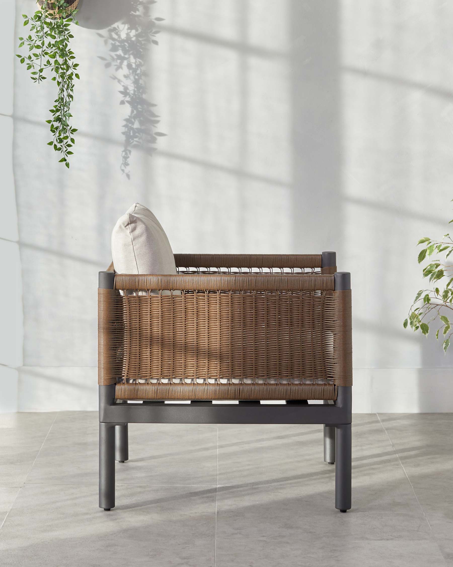 Modern outdoor armchair with a dark grey metal frame and woven brown rattan backrest and sides, featuring a single light beige cushion on the seat.