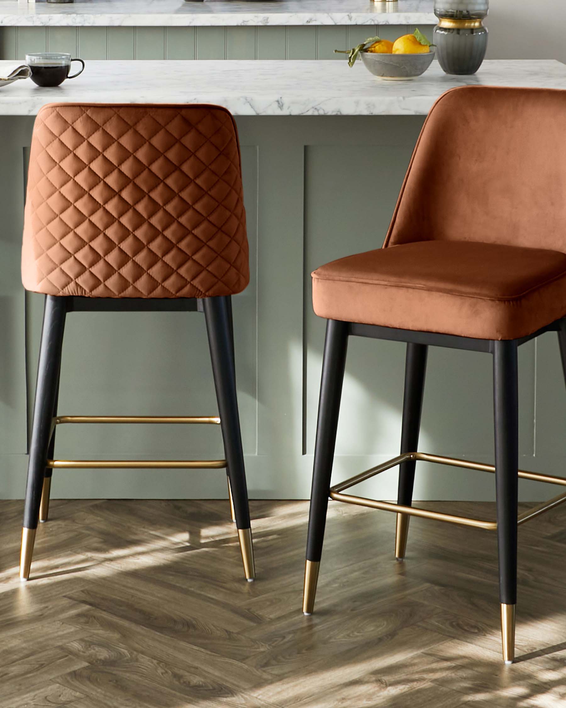 Two modern bar stools with quilted terracotta upholstery and black legs with gold footrests.