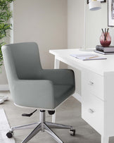 A modern grey office chair with a high backrest and sleek armrests, mounted on a five-point chrome base with casters for mobility. Adjacent to it is a white desk with a minimalist design, featuring clean lines and equipped with two drawers for storage.