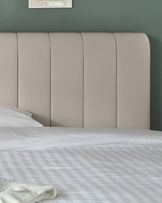 Modern, neutral-toned upholstered headboard with vertical panel design, positioned behind a bed with a patterned white duvet.