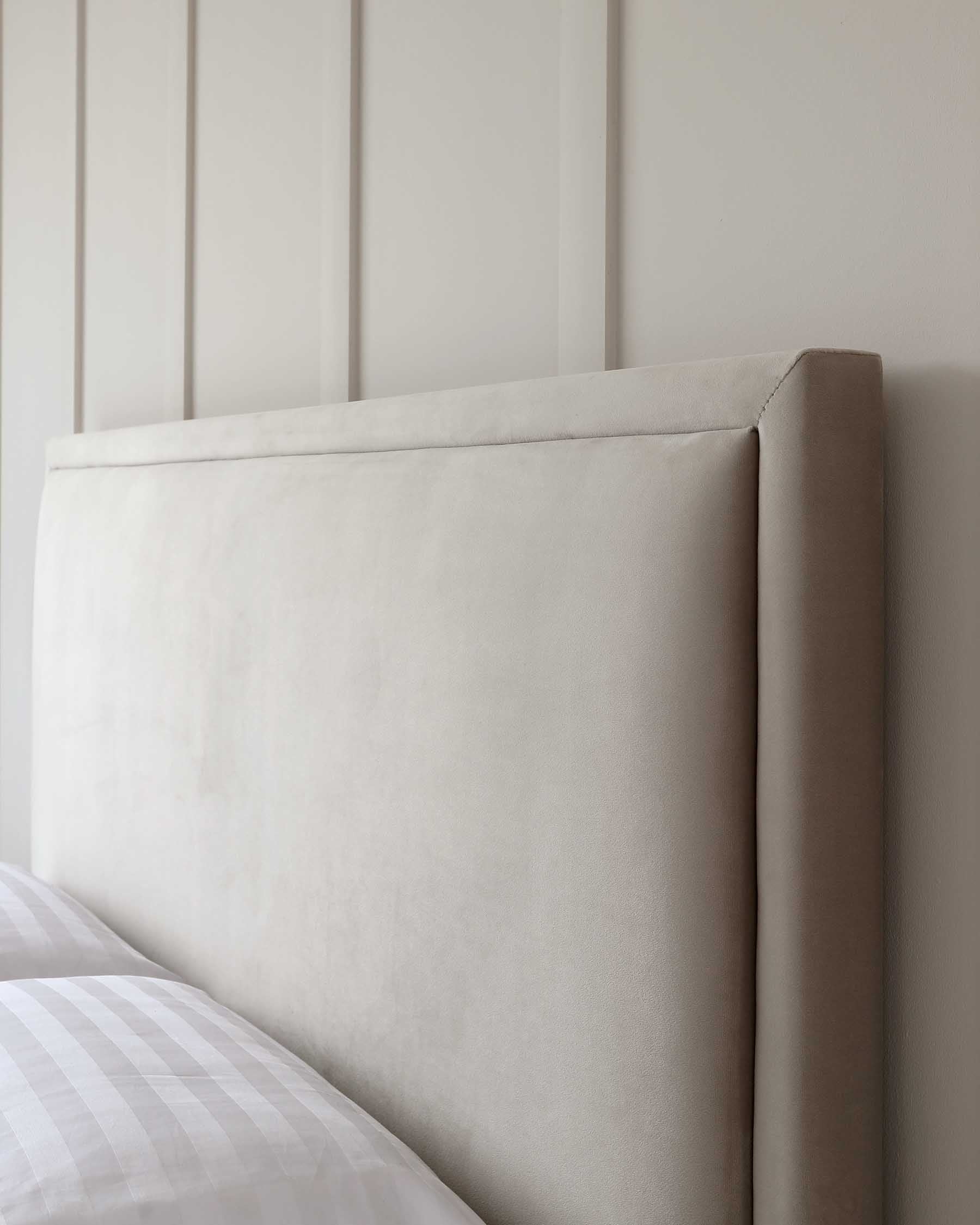 Elegant, minimalist upholstered headboard in a light beige fabric, affixed to a bed with white and grey checkered bedding.