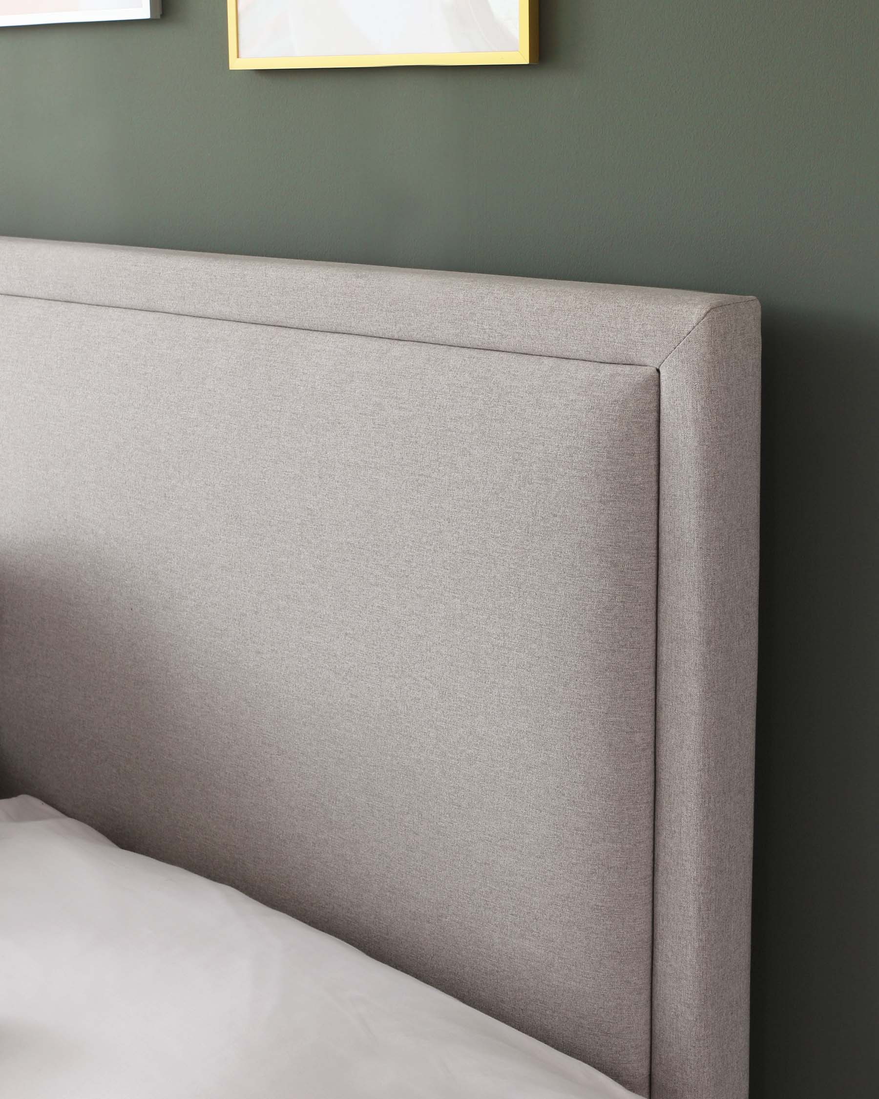 Upholstered light grey fabric headboard with a simple, sleek, padded design, set against a dark green wall, partially obscured by white bedding.