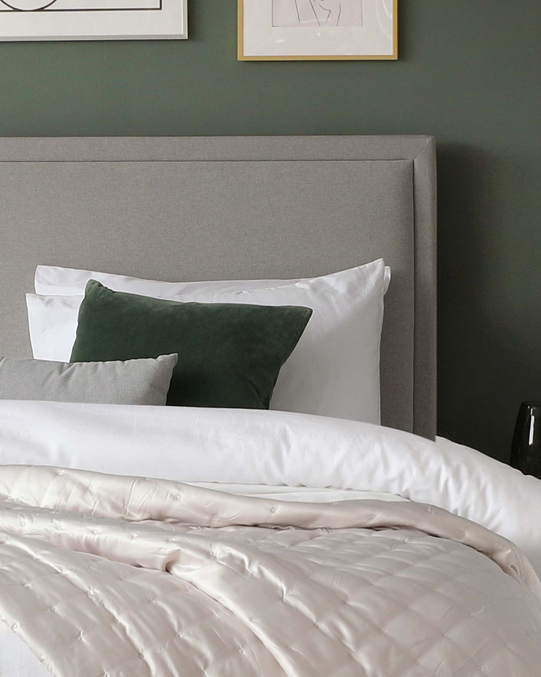 Elegant grey upholstered headboard with a subtle horizontal panel design, part of a bed that's adorned with crisp white bedding and accented by a dark green velvet throw pillow.