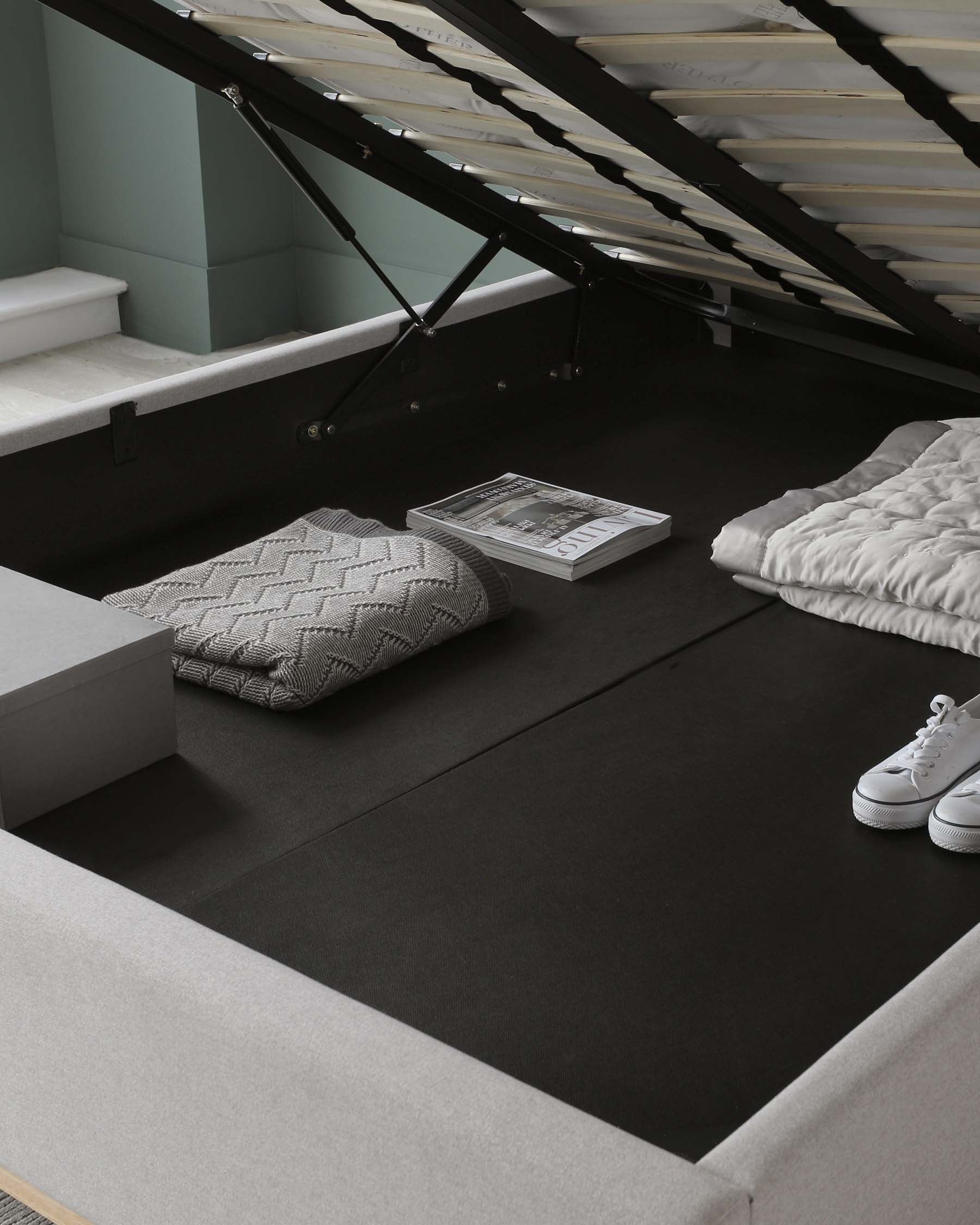 A modern, low-profile platform bed in a minimalist style, featuring a sleek grey upholstered frame without a headboard, and a dark grey or black mattress or bedding surface. The bed is complemented by a textured grey throw pillow and a folded white comforter. The simple, clean lines of the bed emphasize a contemporary aesthetic suitable for a space-saving urban interior.