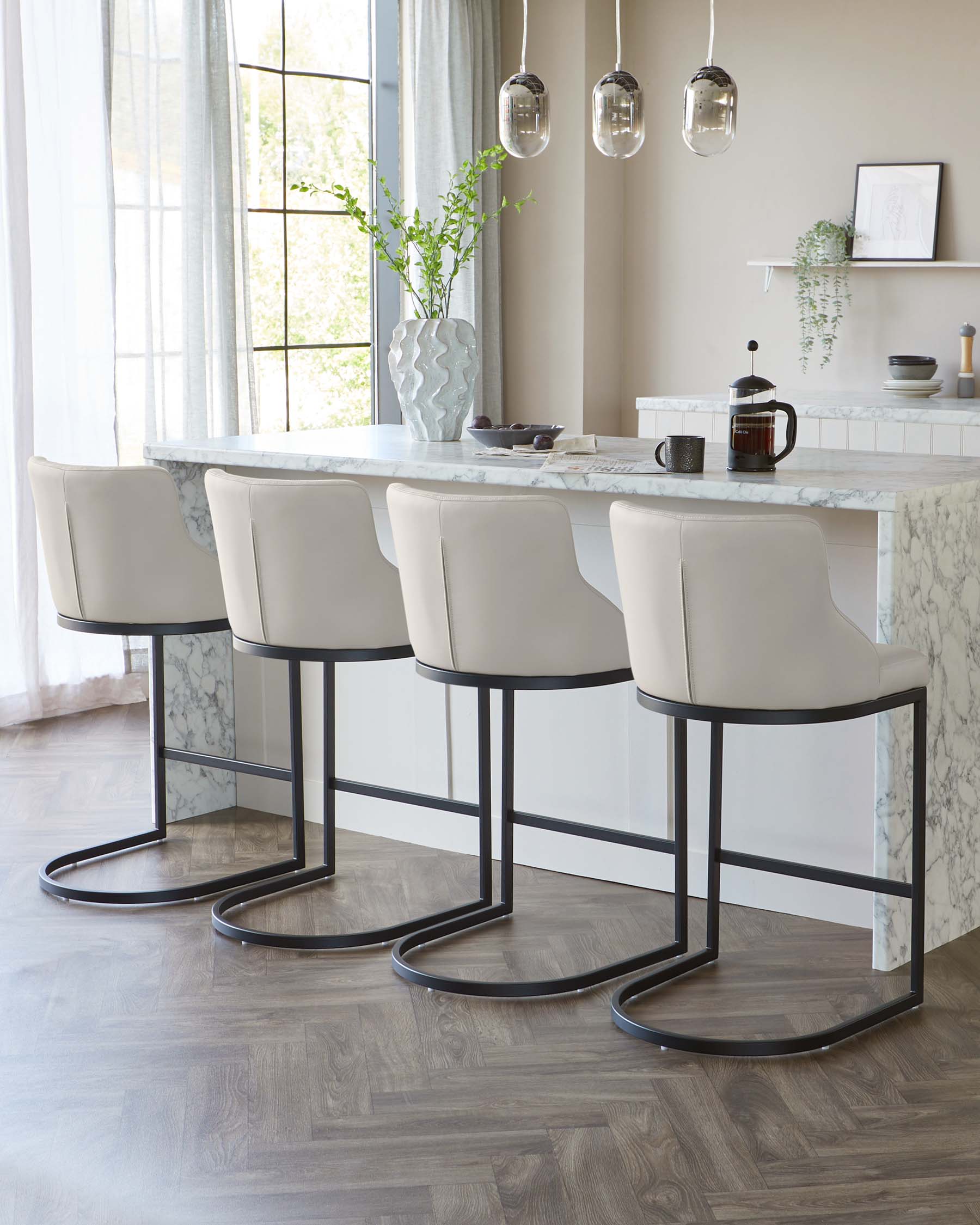 Four modern bar stools with beige upholstered seats and sleek black metal legs arranged at a white marble countertop.