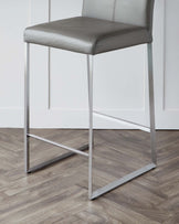 Modern grey leatherette barstool with a high back and sleek metal frame in a room with light wooden flooring and white panelling.