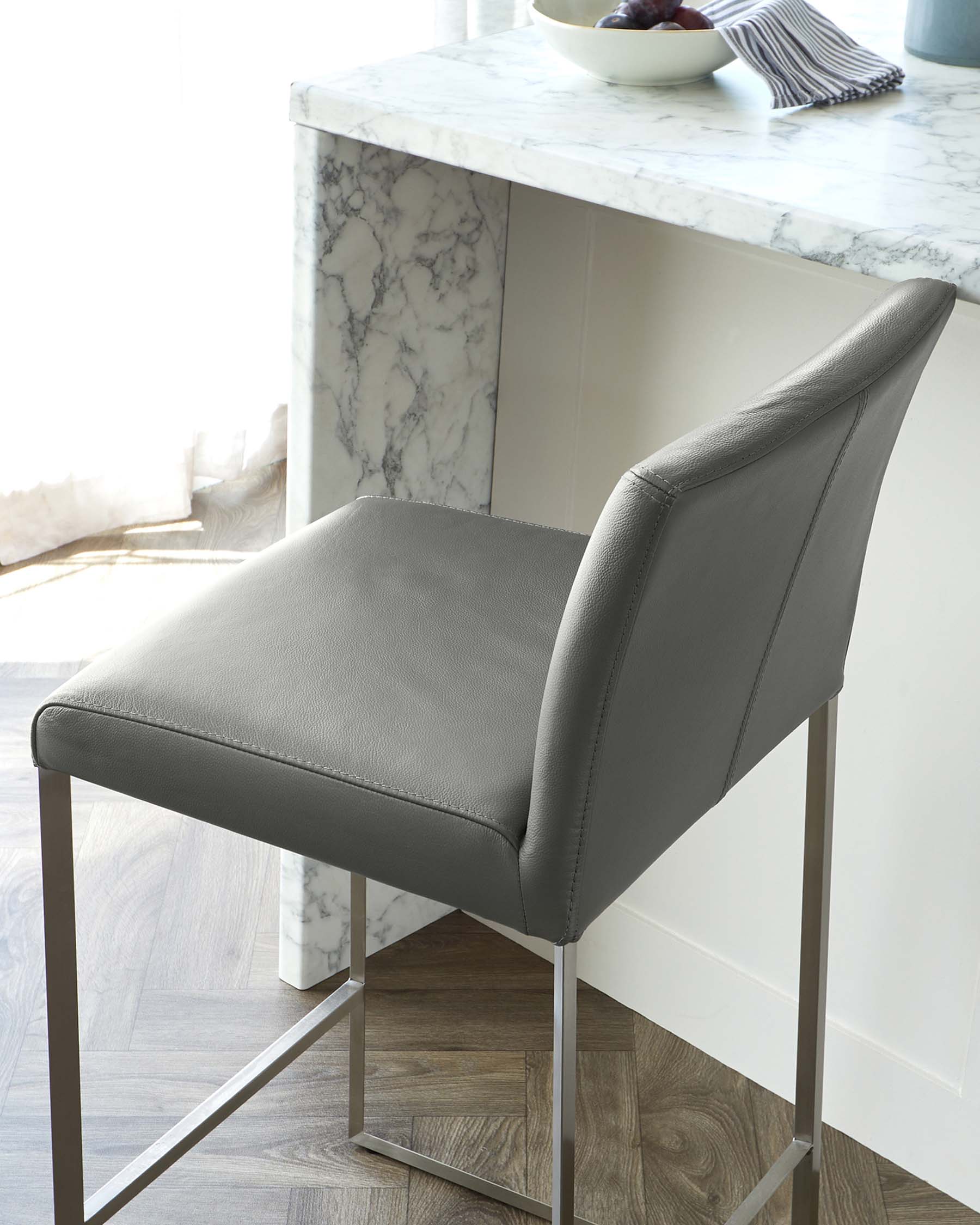 Modern grey faux leather barstool with a low backrest and sleek metal frame, paired with a white marble countertop kitchen island.