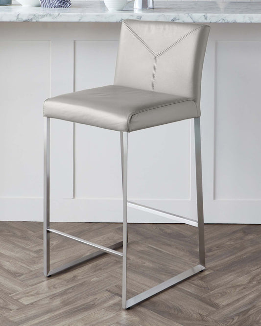 Modern bar stool with a sleek design, featuring a taupe leatherette seat and backrest with a decorative stitched detailing, supported by slender chrome-finished metal legs forming a square base for stability.