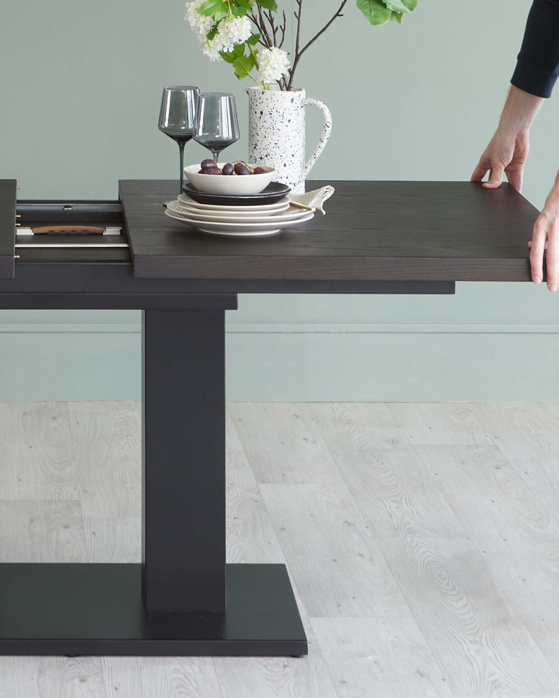 Modern extendable dining table in a dark finish with a rectangular tabletop and a solid, minimalist base showcasing a sleek silhouette.