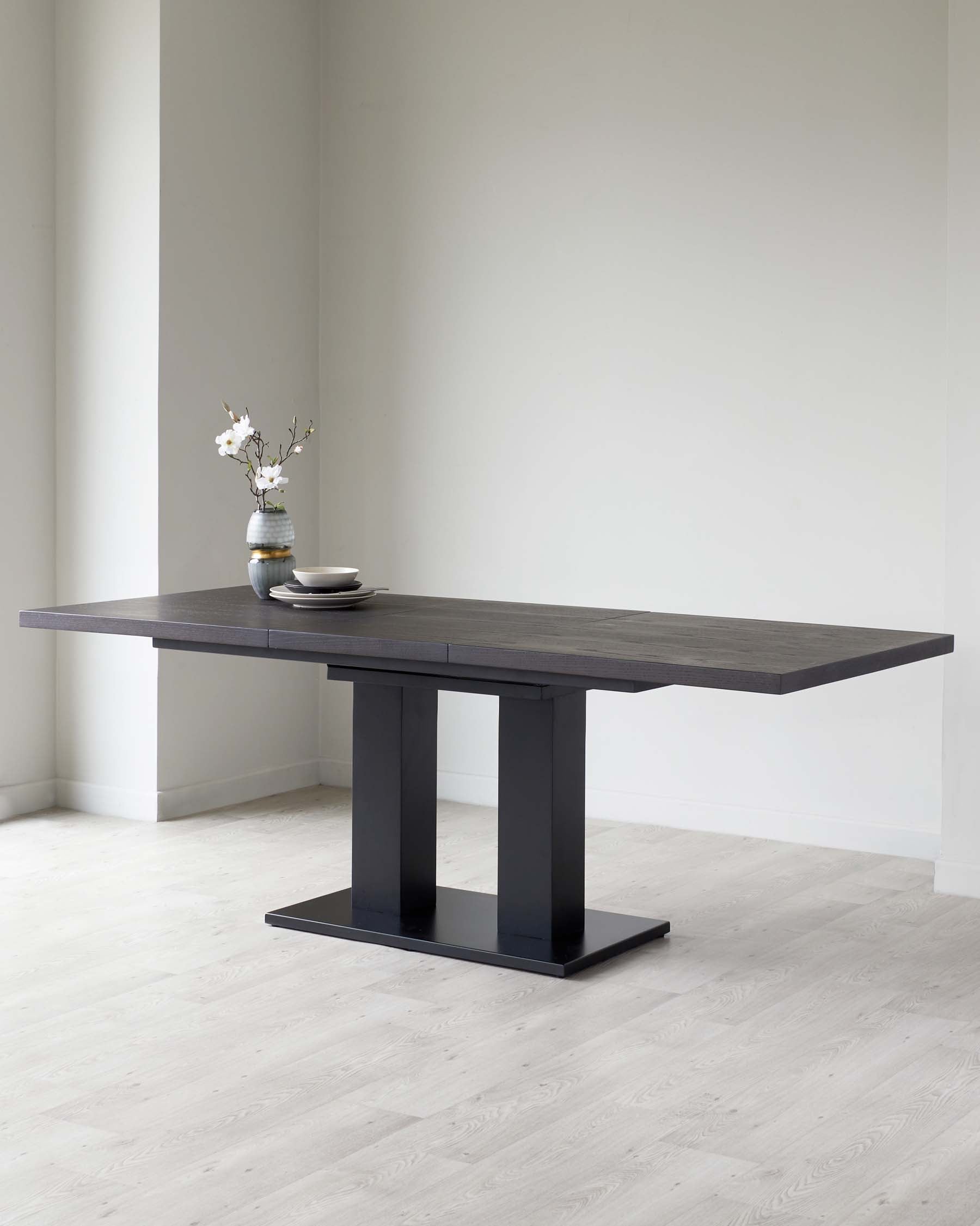 Modern minimalist dark wood dining table with a rectangular top and a sturdy trestle base, accented with a decorative flower vase and set of plates.