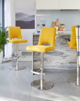 Modern adjustable-height swivel bar stools with mustard yellow upholstery and cushioned seats and backs, featuring sleek metal bases with circular footrests.