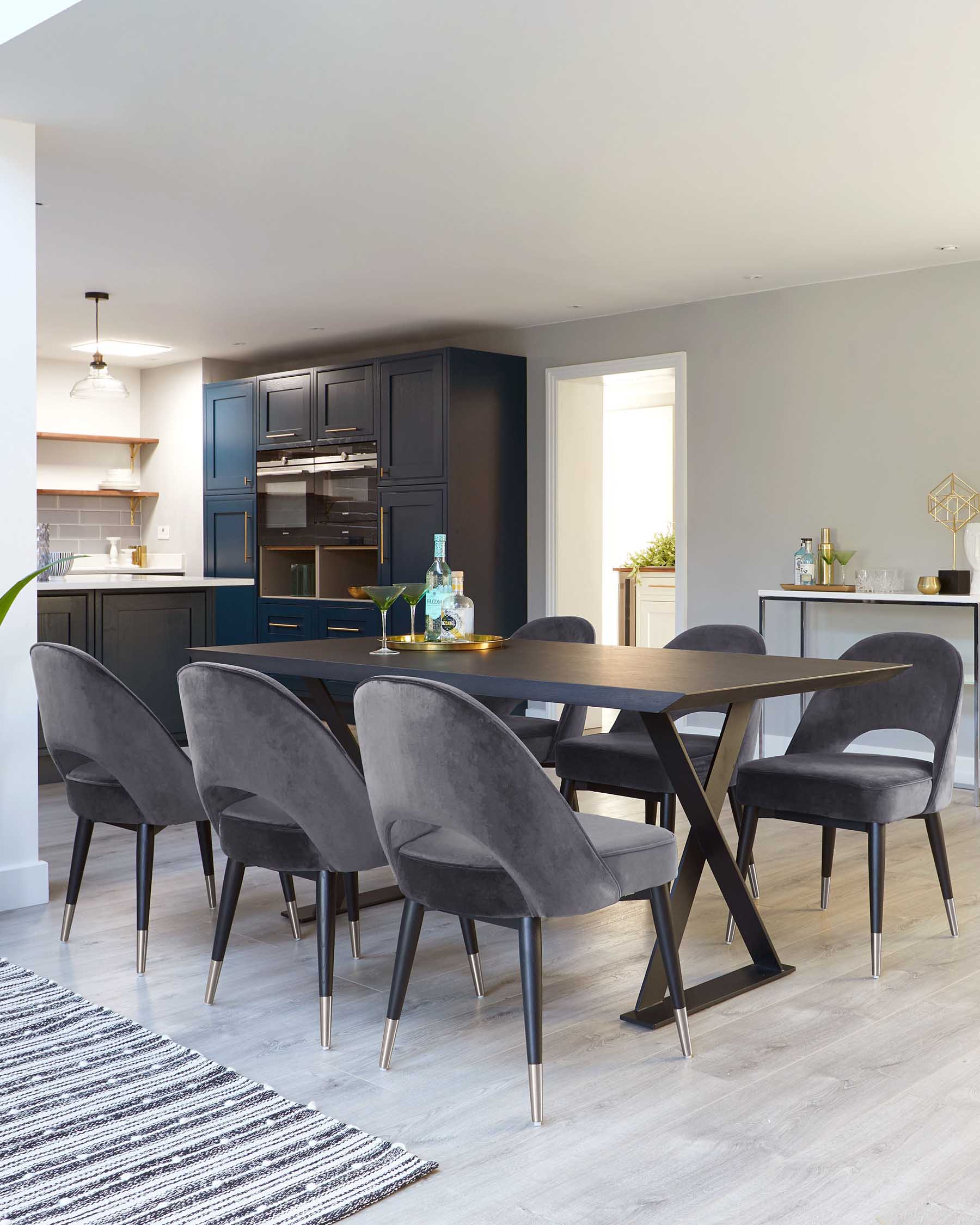 A modern dining room set featuring a dark wood rectangular table with an X-shaped base. Surrounding the table are six plush velvet-upholstered chairs with sleek metal-tipped legs, giving a luxurious yet contemporary feel to the space.