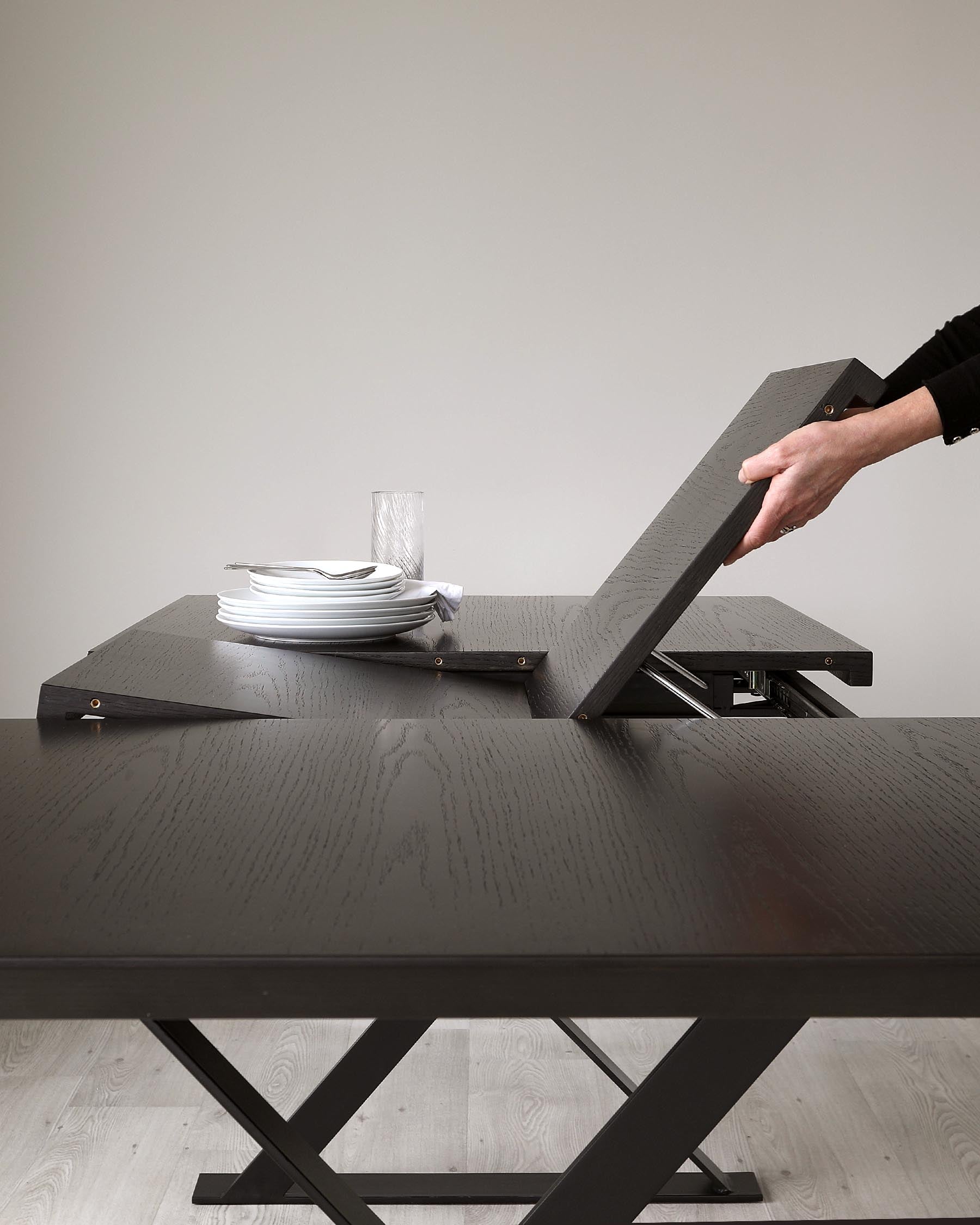 Modern extendable dark wood dining table with a unique mechanism, featuring a textured surface and an angular crossed leg design, partially extended to display functionality.