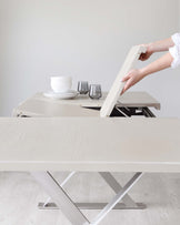 Stylish light wood table with extendable top and modern metal base, featuring white dishes and gray glassware on display.