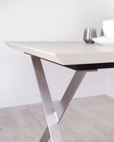 Modern dining table with a sleek light wood surface and stylish metal X-frame legs, complemented by elegant dishware.