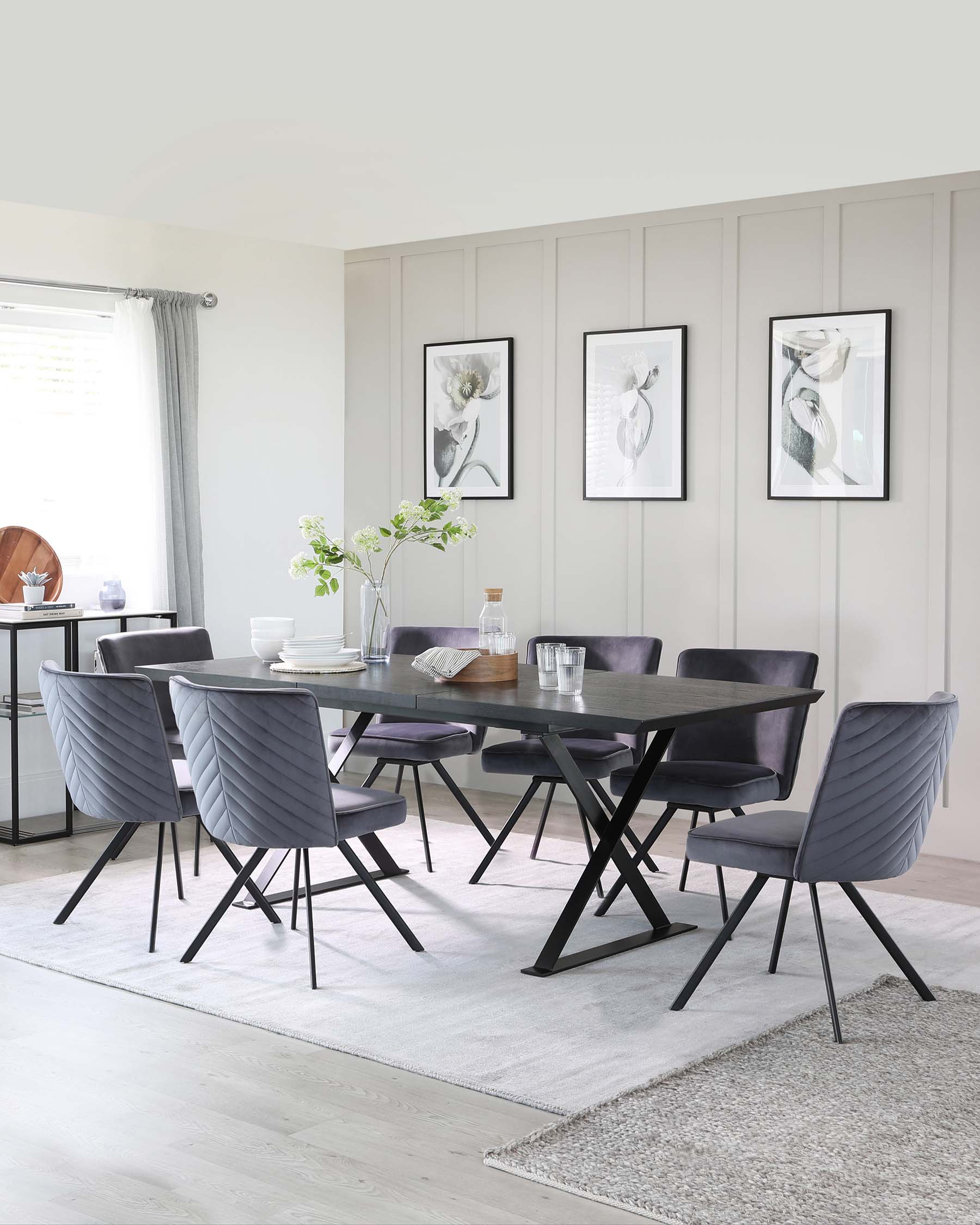 A modern dining room set featuring a sleek, rectangular table with a dark finish and a distinctive X-shaped leg design. Accompanying the table are six contemporary chairs with channel-tufted upholstery in a muted grey tone, featuring slim, black metal legs that match the table. The set is arranged on a light grey area rug, providing contrast to the dark furniture.