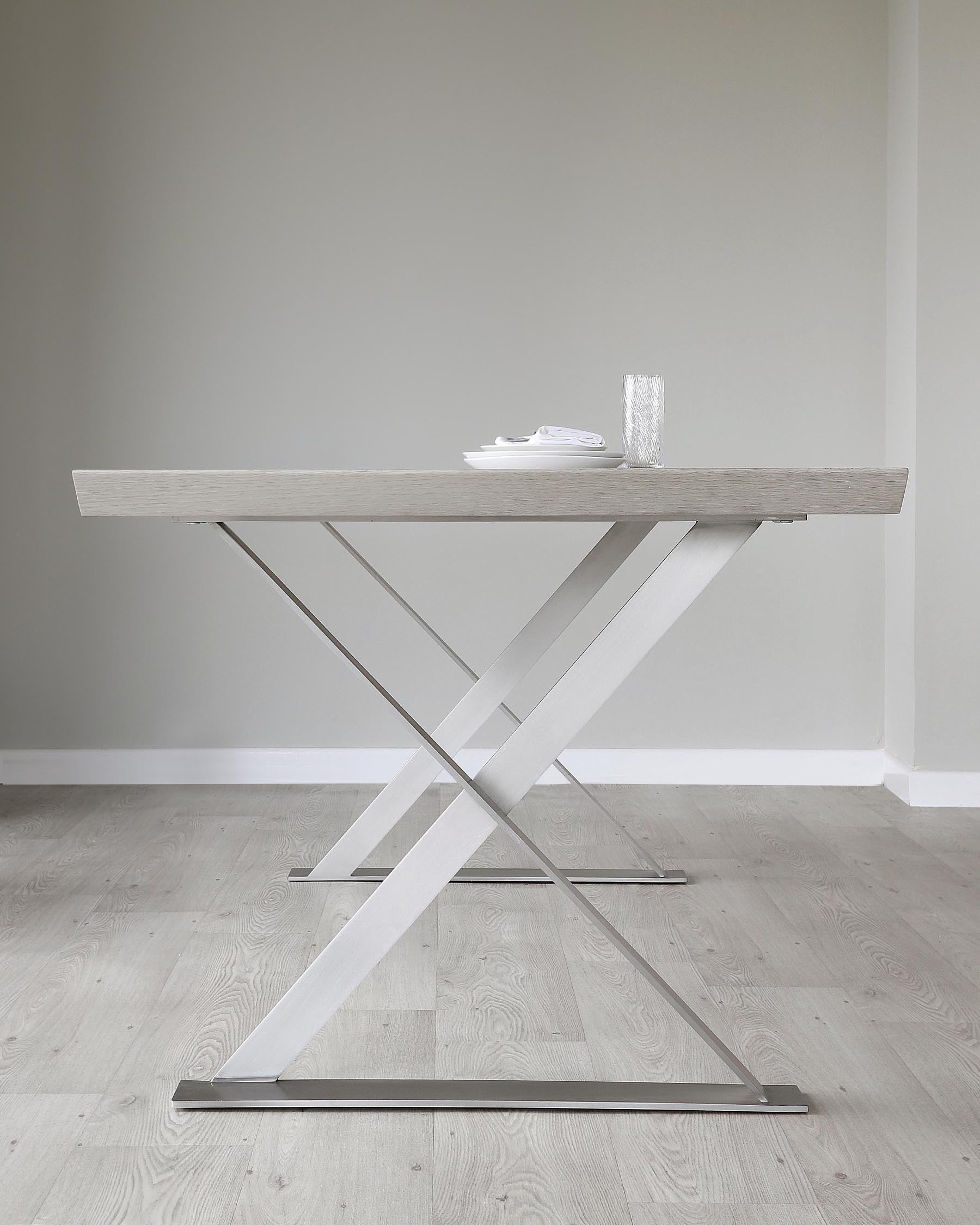 Modern minimalist dining table with a light wood grain finish and striking white crisscross metal legs, set against a neutral interior backdrop.