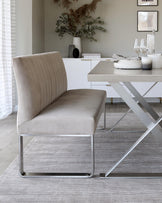 Elegant modern dining furniture featuring a light taupe upholstered chair with vertical stitching on the backrest and a sleek chrome base, paired with a white dining table with a unique intersecting chrome leg design.