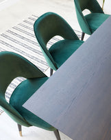 Modern wood-grain dining table paired with elegant dark green velvet upholstered chairs with a unique rounded backrest design, set on a grey and white striped area rug.