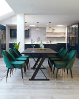 Modern dining room featuring a dark wood table with a geometric black metal base, surrounded by six luxurious teal velvet upholstered chairs with black legs tipped with gold accents. The room has a contemporary aesthetic with a mix of sophisticated colours and warm wood tones.