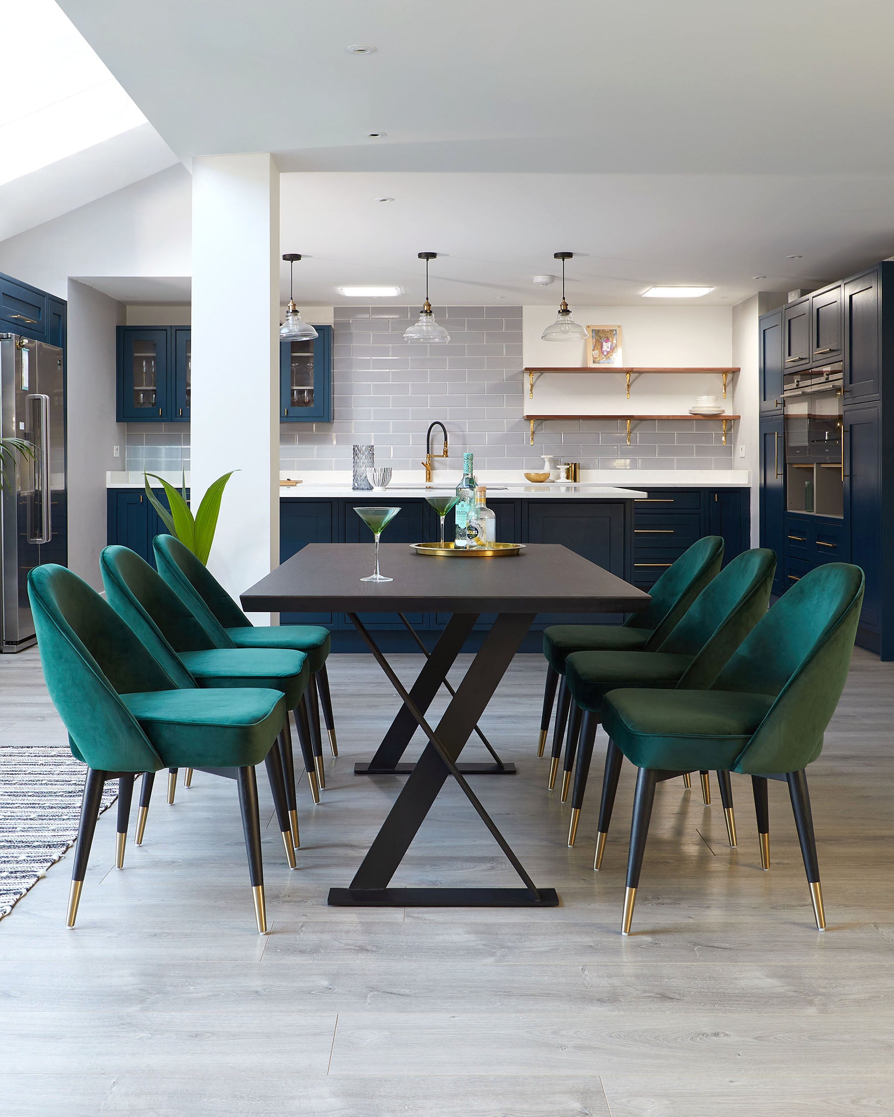 Contemporary dining set featuring a rectangular table with a matte black top and unique X-shaped legs in a contrasting black and gold design, accompanied by six plush velvet dining chairs in a striking emerald green, each with elegant, vertical backrest stitching and slim black legs tipped with gold accents.