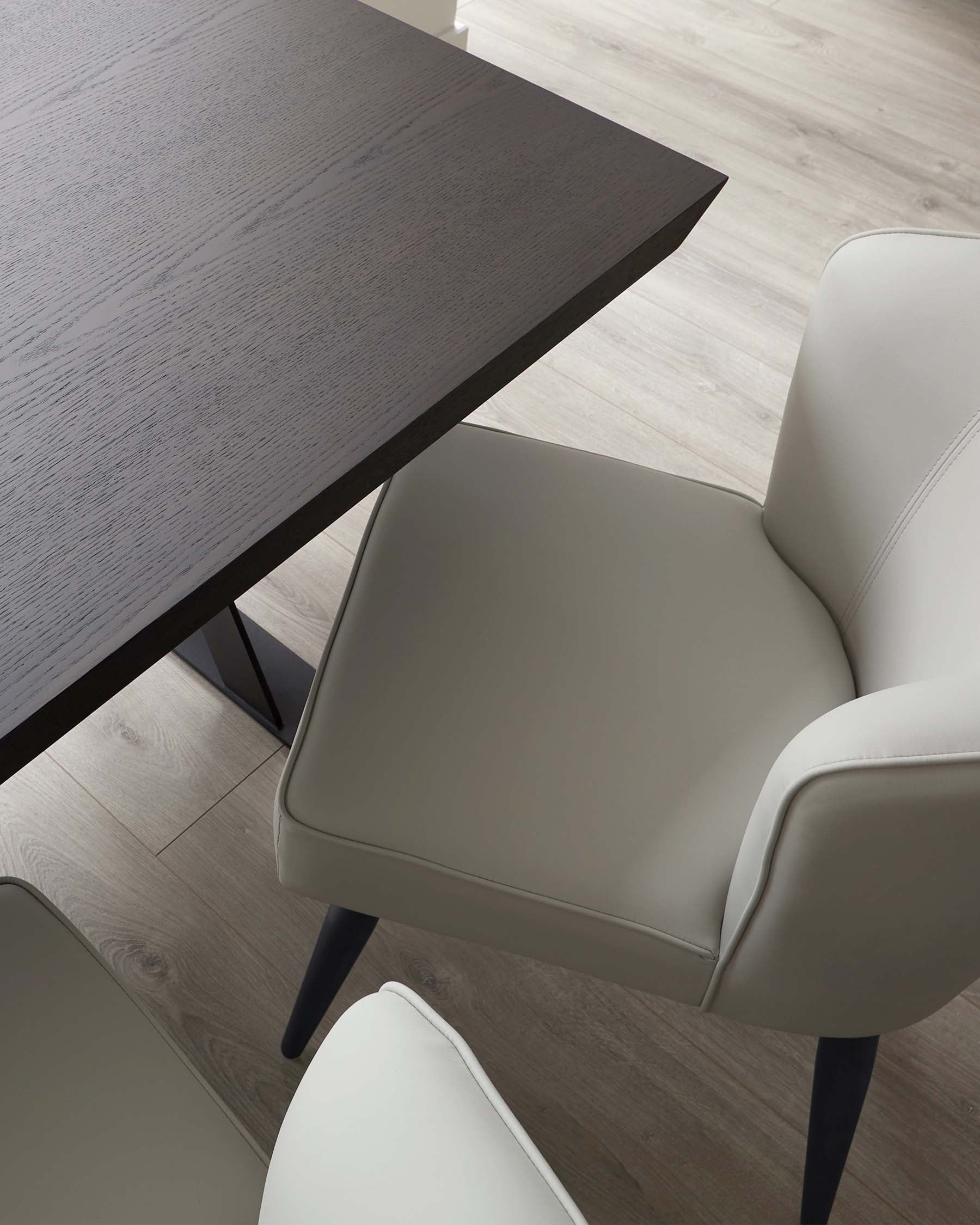 Contemporary dining setup featuring a minimalist dark wood table with pronounced wood grain and angled metal legs accompanied by sophisticated light grey upholstered chairs with sleek lines and dark wooden legs.