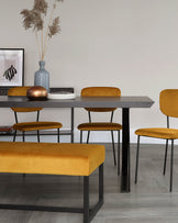 A contemporary dining set featuring a wooden table with a dark, textured finish and slender black metal legs, accompanying mustard yellow upholstered chairs with a smooth fabric finish and same black metal leg design, and a matching bench with plush upholstery and a minimalist metal frame beneath.