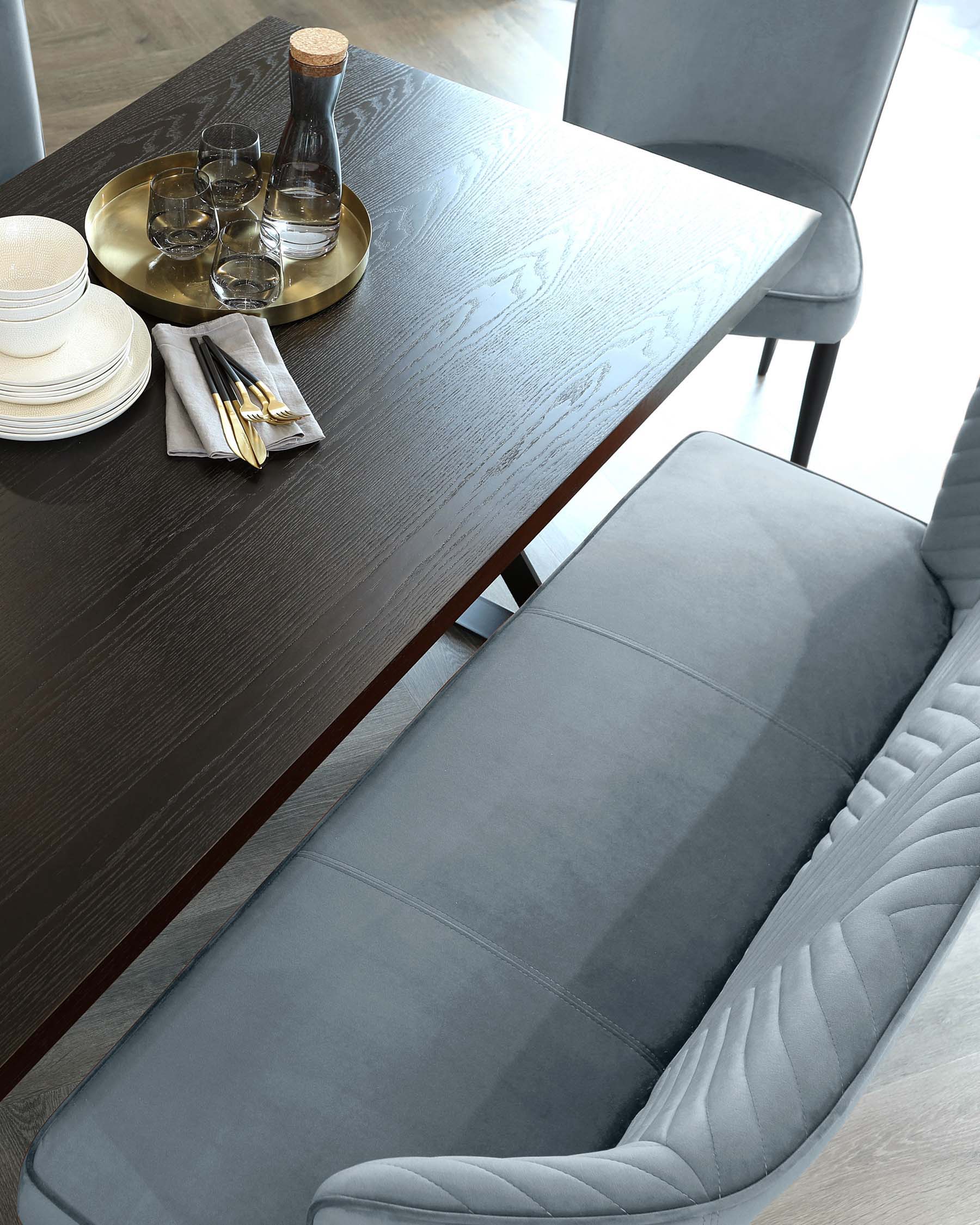 A sleek dark wood dining table with a plush light blue bench and gray upholstered chairs, complemented by stylish tableware.