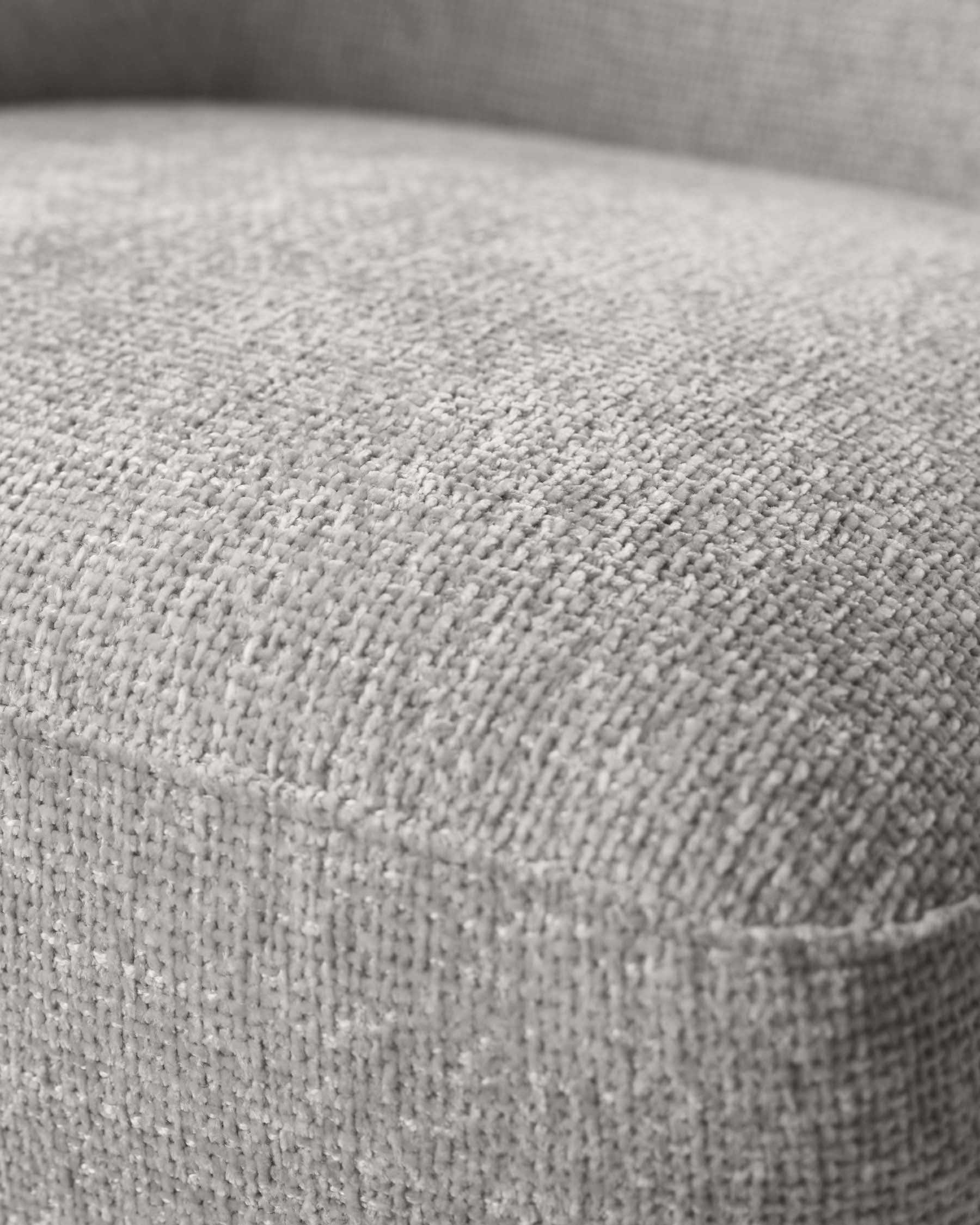 Close-up texture detail of a light grey upholstered furniture piece, highlighting the tightly woven fabric and the soft curvature of the cushioned surface.