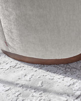 Close-up view of a modern light fabric upholstered chair with a sleek wooden base, placed on a textured light-coloured rug.