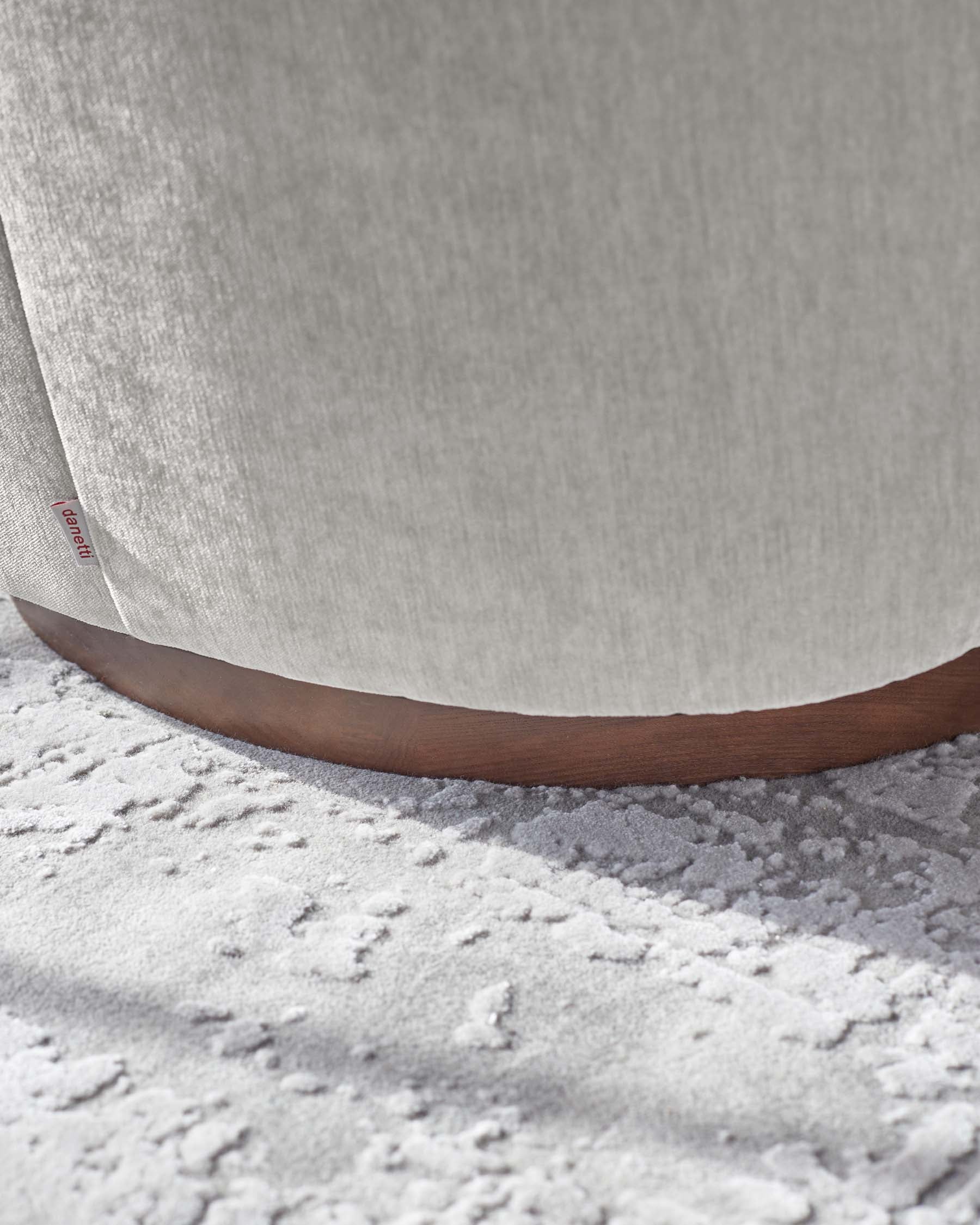 Close-up view of a modern light fabric upholstered chair with a sleek wooden base, placed on a textured light-coloured rug.