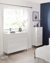 A contemporary white bedroom furniture set including a drawer dresser and a 5-drawer tall chest. Both pieces feature a modern geometric textured front, sleek metal legs, and minimalist handles.