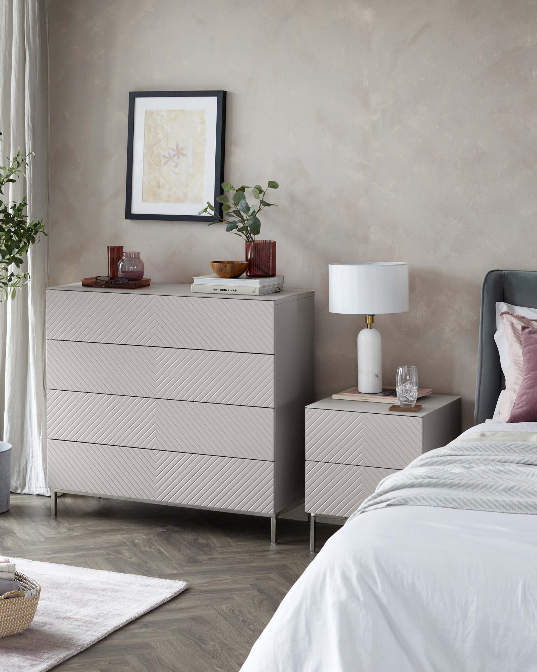 Contemporary bedroom furniture set featuring a light grey wood-textured finish with a modern chevron pattern. Includes a six-drawer dresser and a two-drawer nightstand with sleek metal handles and slim metal legs. A matching lamp with a white shade sits atop the nightstand.