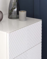 White modern dresser with a textured chevron pattern on its front, set against a navy blue wall.