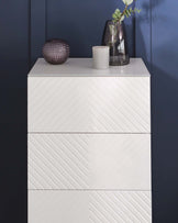 Modern white four-drawer dresser with a chevron pattern, against a dark blue wall.