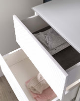 A modern white dresser with an open drawer revealing neatly folded clothes, showcasing the spacious and clean-lined design of the storage furniture.