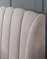 Close-up of a modern beige upholstered headboard with vertical channel tufting.