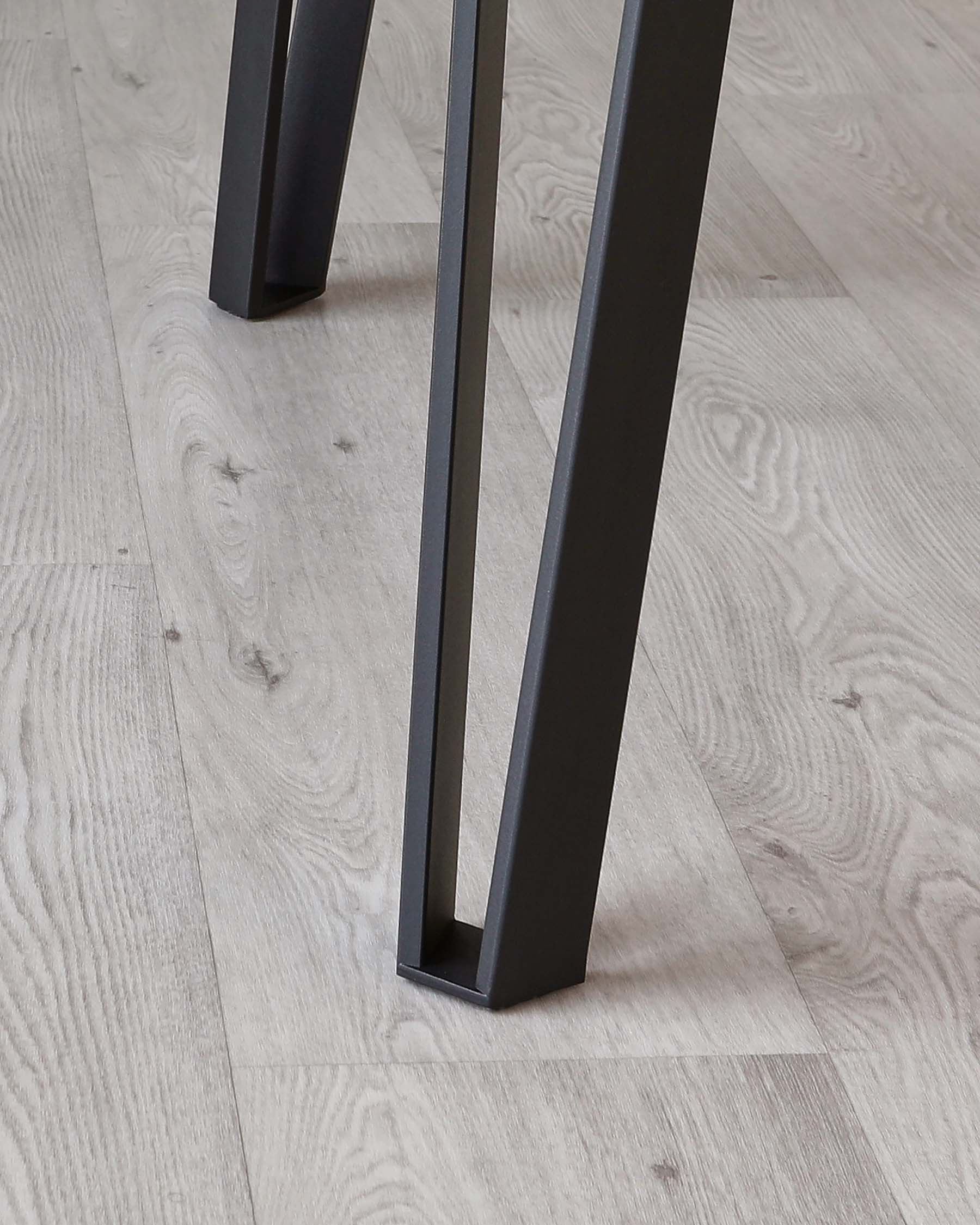 Close-up view of modern furniture legs in matte black on a pale wooden floor, showcasing sleek, minimalistic design with clean lines.