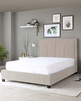 A modern beige upholstered platform bed with a large, cushioned headboard featuring an elegant chevron pattern. The bed is situated on a light grey area rug, and there are no visible linens or pillows on the mattress.