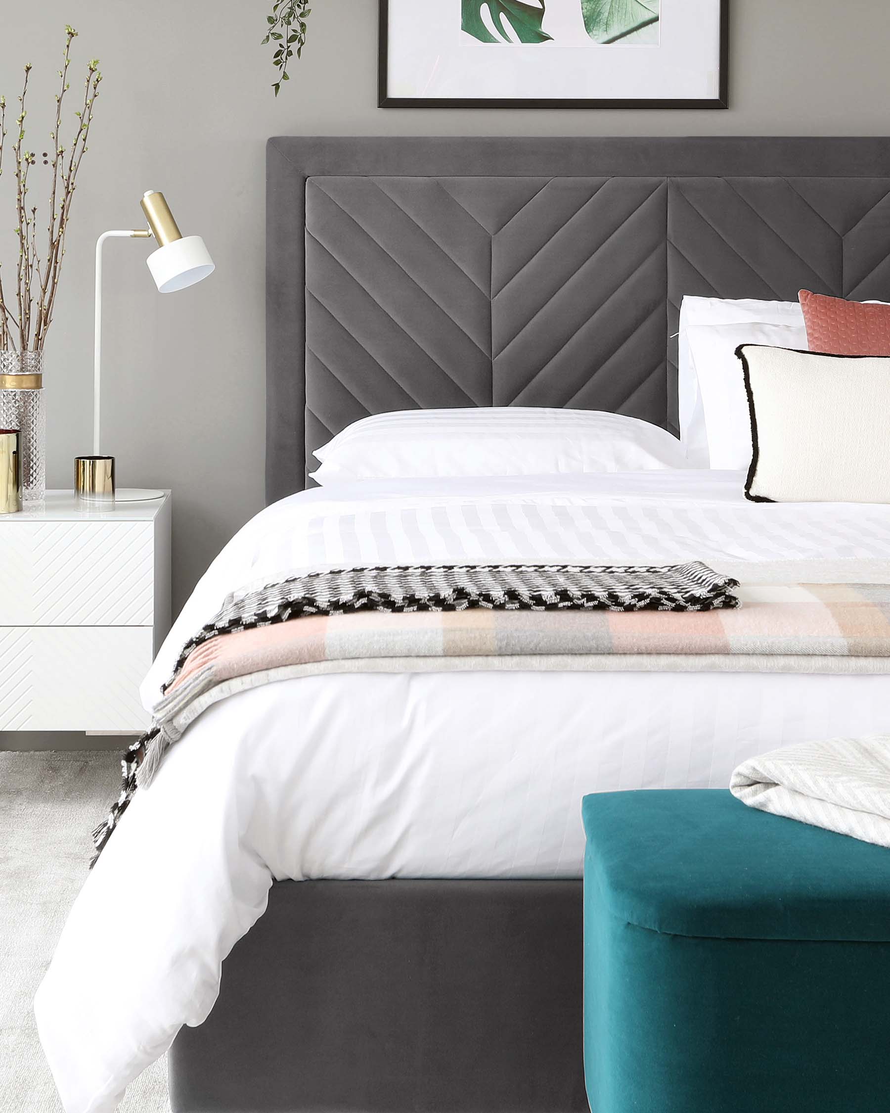 Modern bedroom furniture including a grey upholstered bed with a geometrically patterned headboard, white nightstand with a chevron pattern, and a round teal ottoman at the foot of the bed.