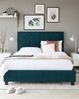 Elegant teal upholstered bed frame with a tufted, high headboard and a plush, white bedding set. Two modern white bedside tables with sleek gold handles flank the bed, each featuring a contemporary white lamp with gold accents. The bedroom setting includes a soft grey rug and white fuzzy slippers at the foot of the bed, creating a cosy and luxurious atmosphere.