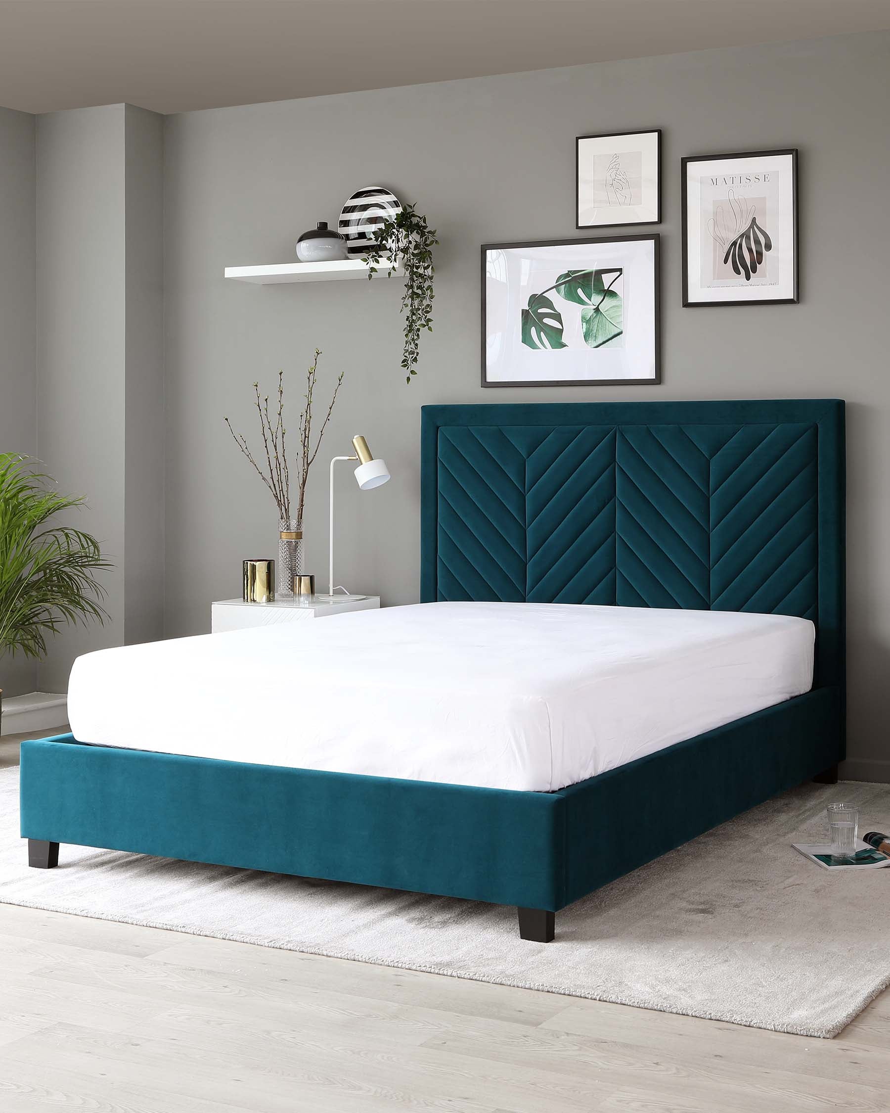 Elegant teal upholstered platform bed featuring a tall headboard with geometric channel tufting on a solid-coloured frame, paired with a simple white floating shelf above and a minimalist style white bedside lamp.