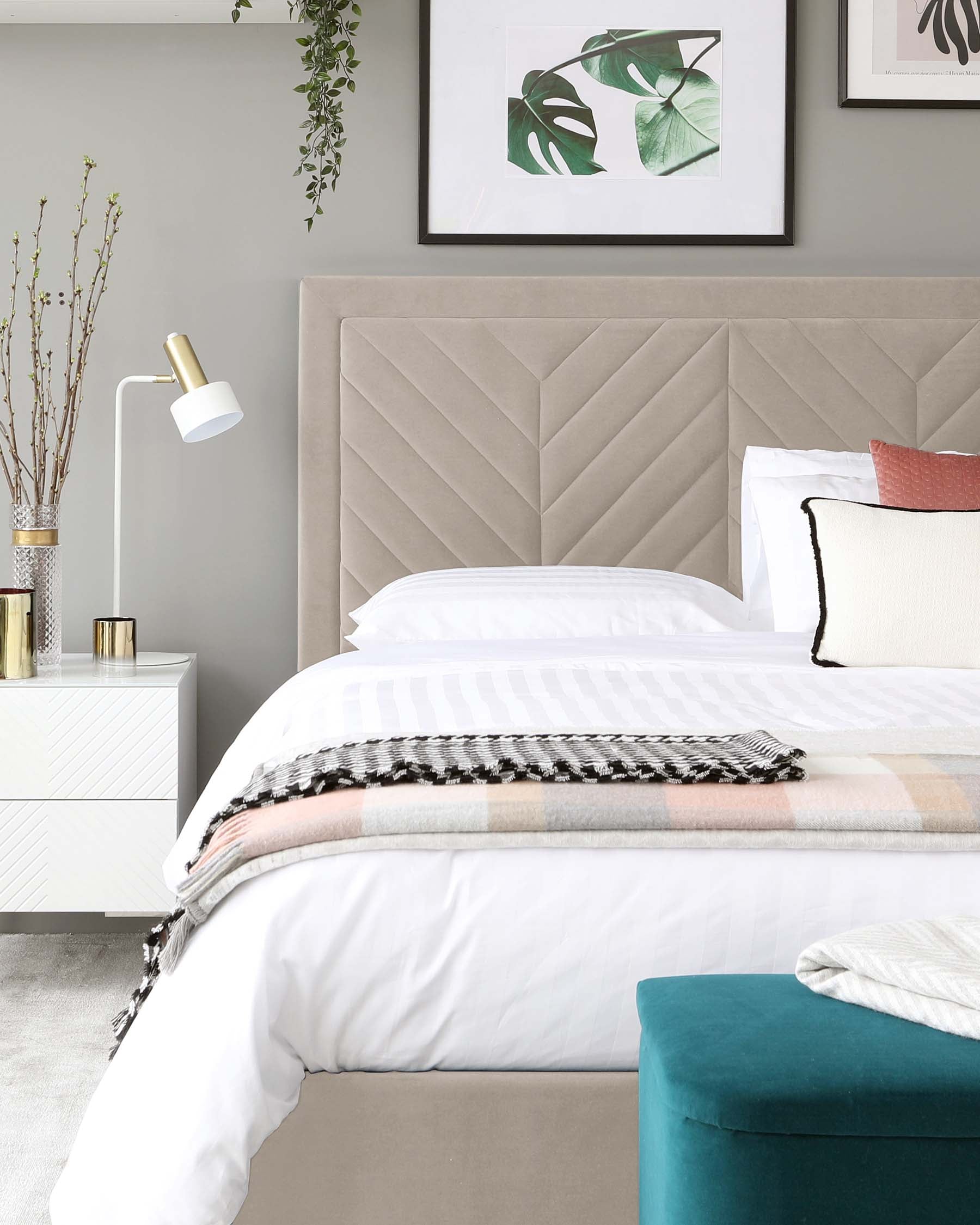 Modern bedroom furniture featuring a large bed with a plush, taupe upholstered headboard showcasing an elegant herringbone pattern. A sleek, white nightstand with brass accents sits beside the bed, complemented by a soft teal ottoman with a velvety texture at the foot of the bed.